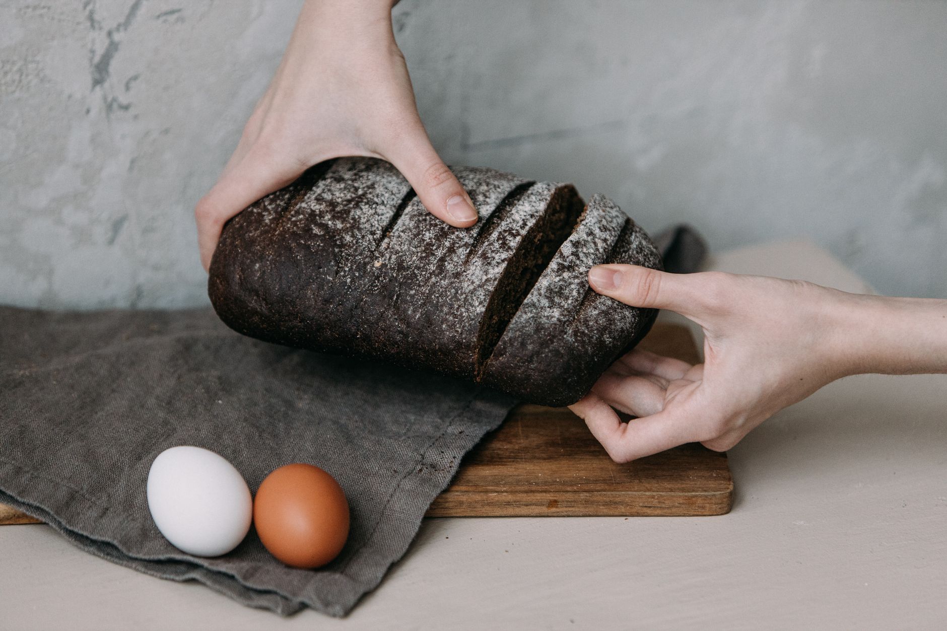 Hands slicing dark rye bread with eggs on a wooden board, perfect for breakfast themes.