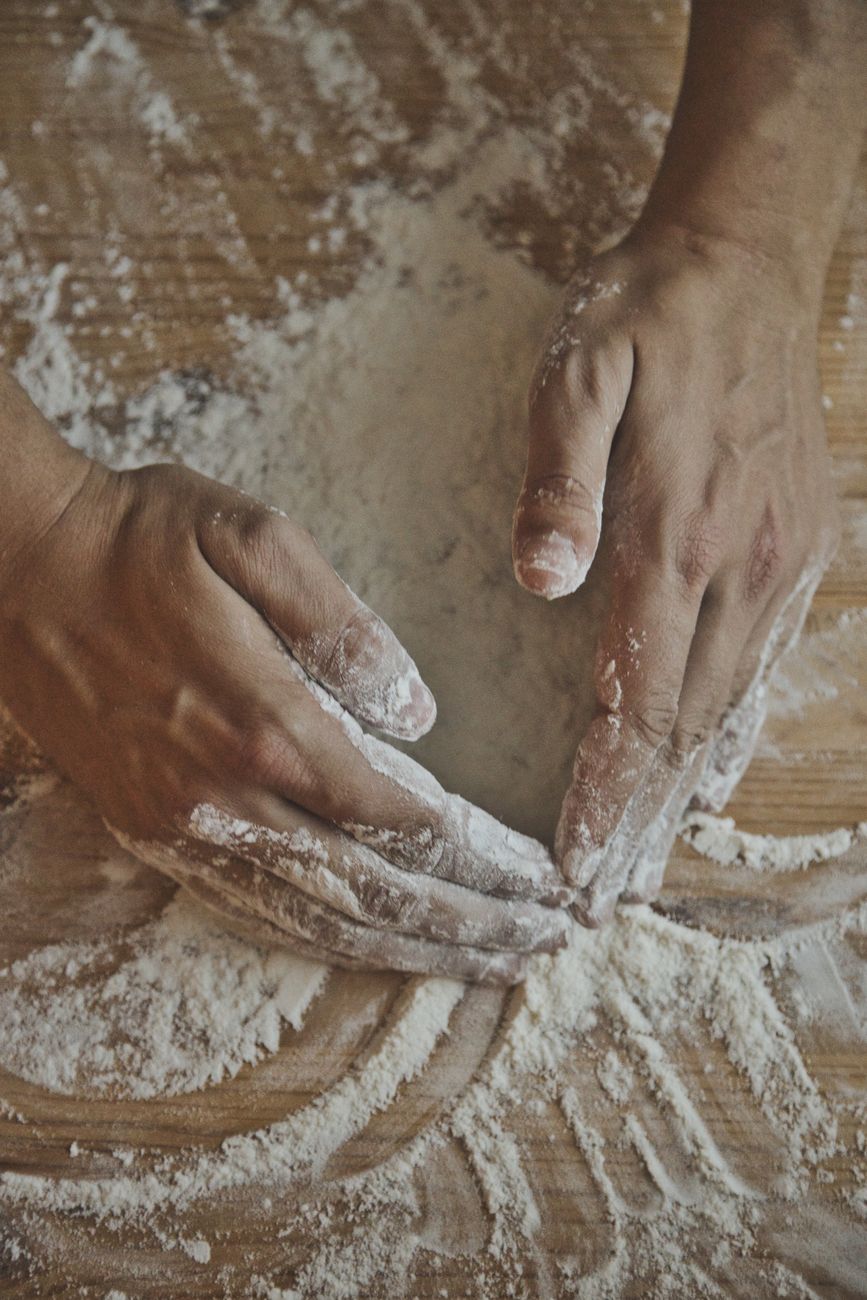 Close-up of hands mixing flour on a wooden board for baking.