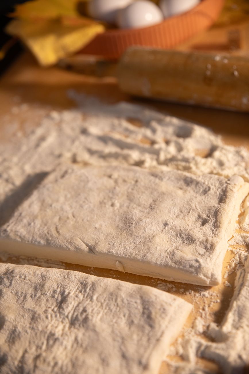 Close-up of rustic puff pastry dough on a floured surface with baking tools.