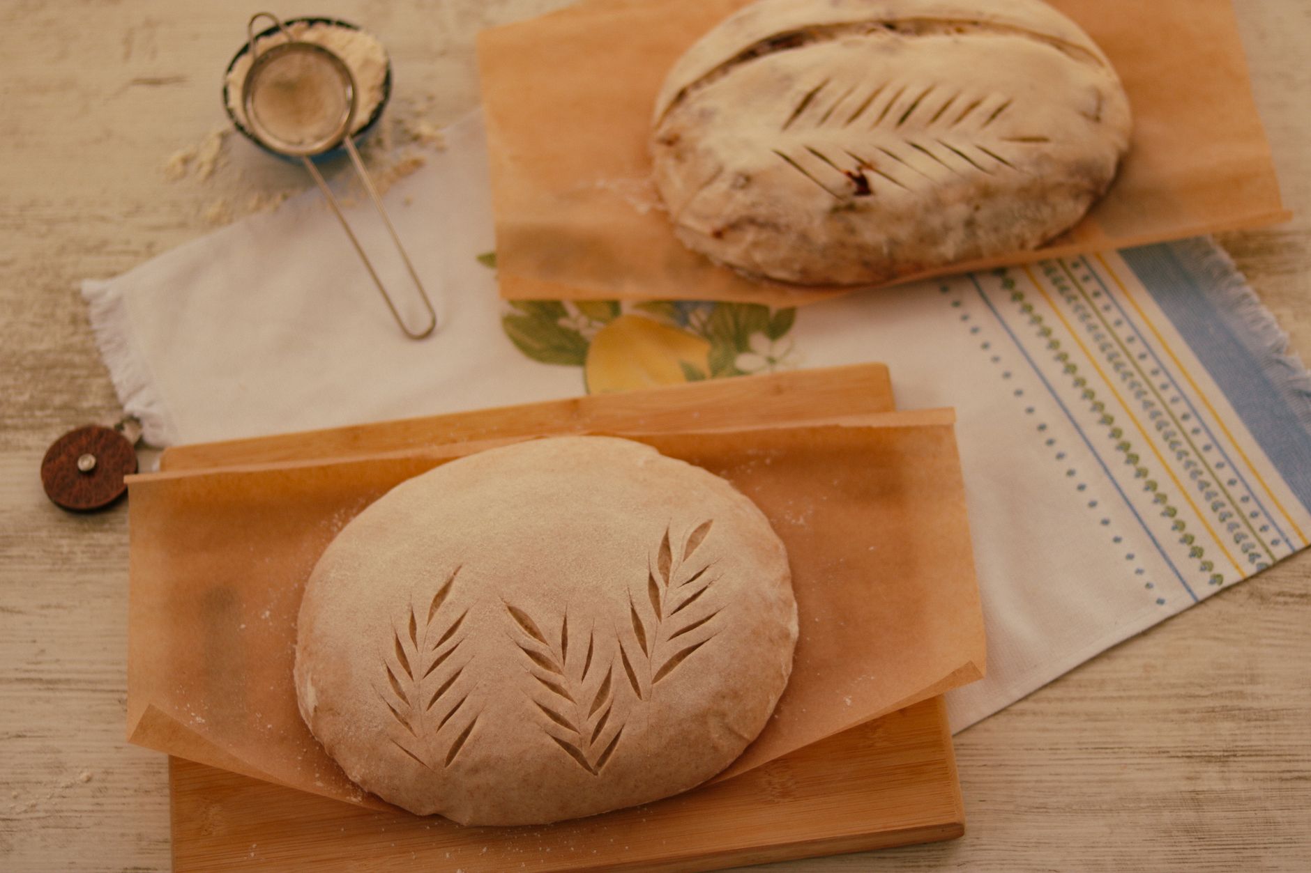 Freshly prepared artisanal bread dough with leaf score patterns on parchment paper.