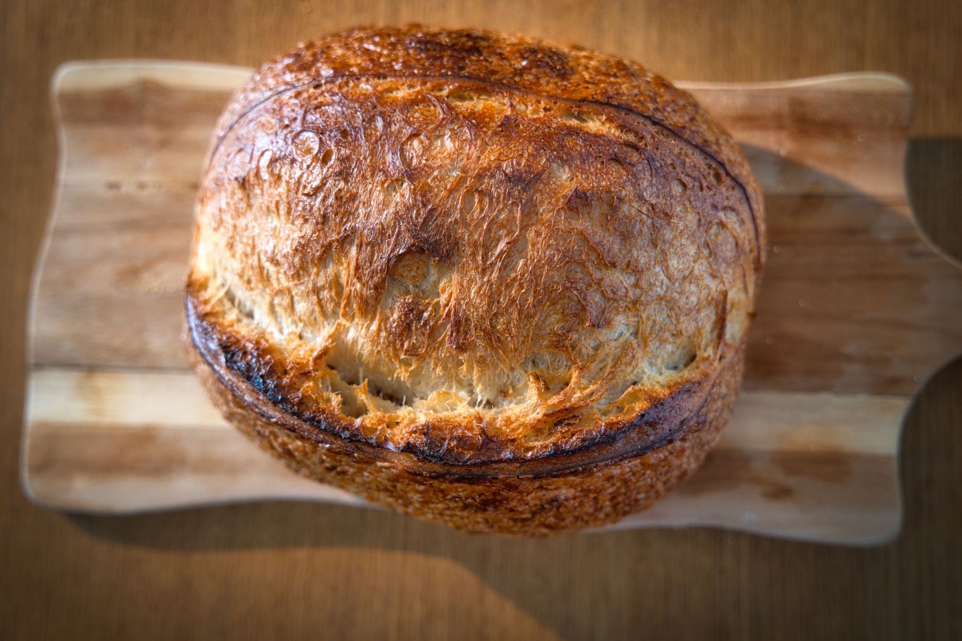 A beautifully baked artisan bread on a wooden cutting board under natural light.